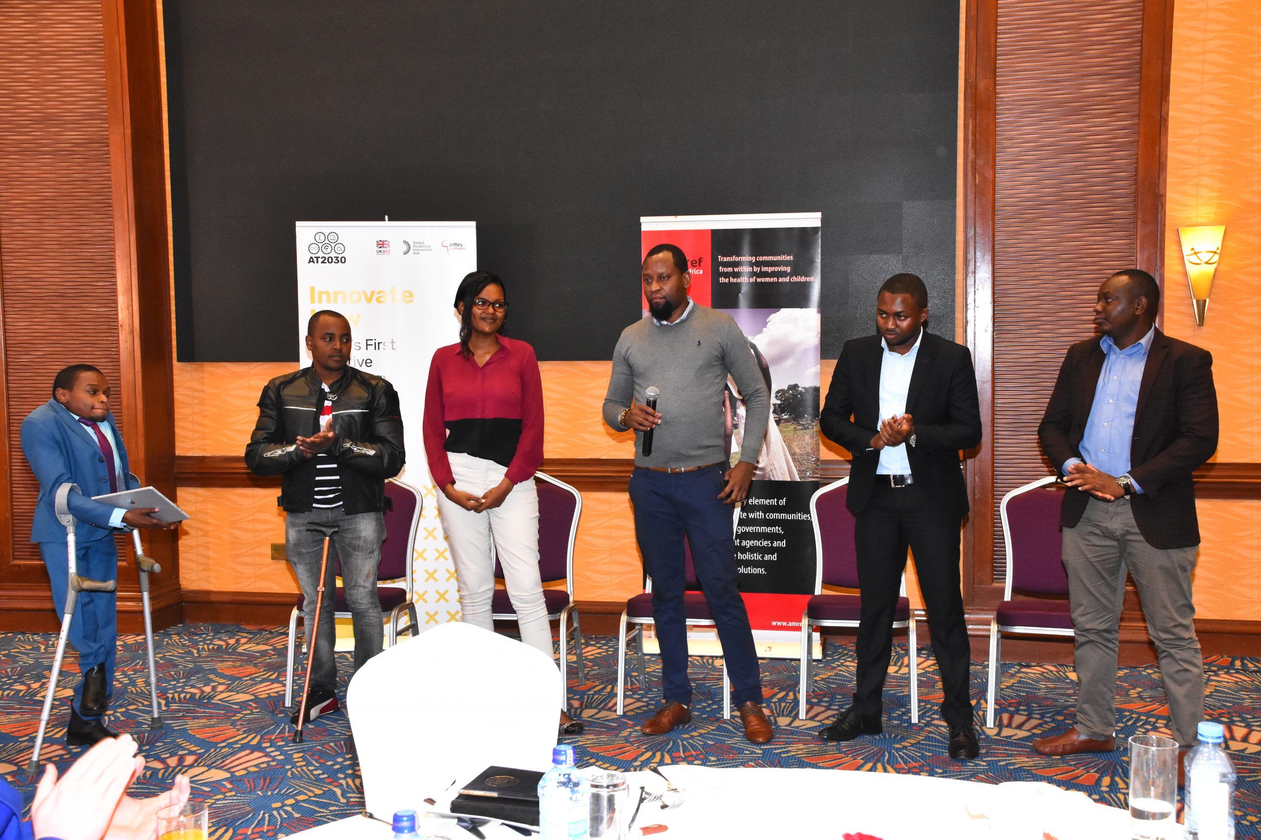 A group of innovators from cohort 1.0 stand in front of an audience